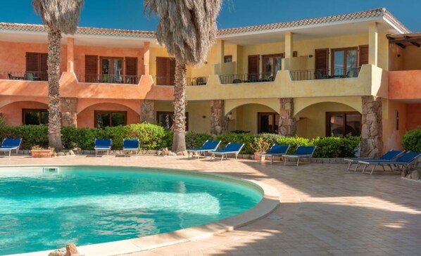 A resort with a swimming pool, sun loungers, and a multi-story building with balconies.