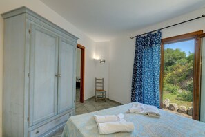 A bedroom with a bed, a wardrobe, a chair, and a view of the outdoors. - Casa Faro Green Village Sardegna (Palau)