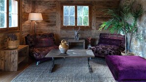 A rustic cabin interior with wooden walls, a sofa, a table, and a lamp.