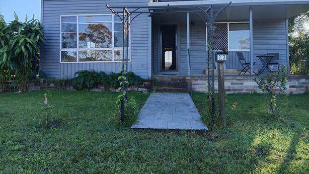 A residential house with a grey exterior, a front porch with a small table and chairs, and a mailbox with the number 23. - The Wonky House (Bowraville)