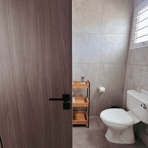 A bathroom with a toilet, a wooden shelf with a plant, and a window. - Nissi Avenue 64 Studio 1 - Luxcyservices (Ayia Napa)