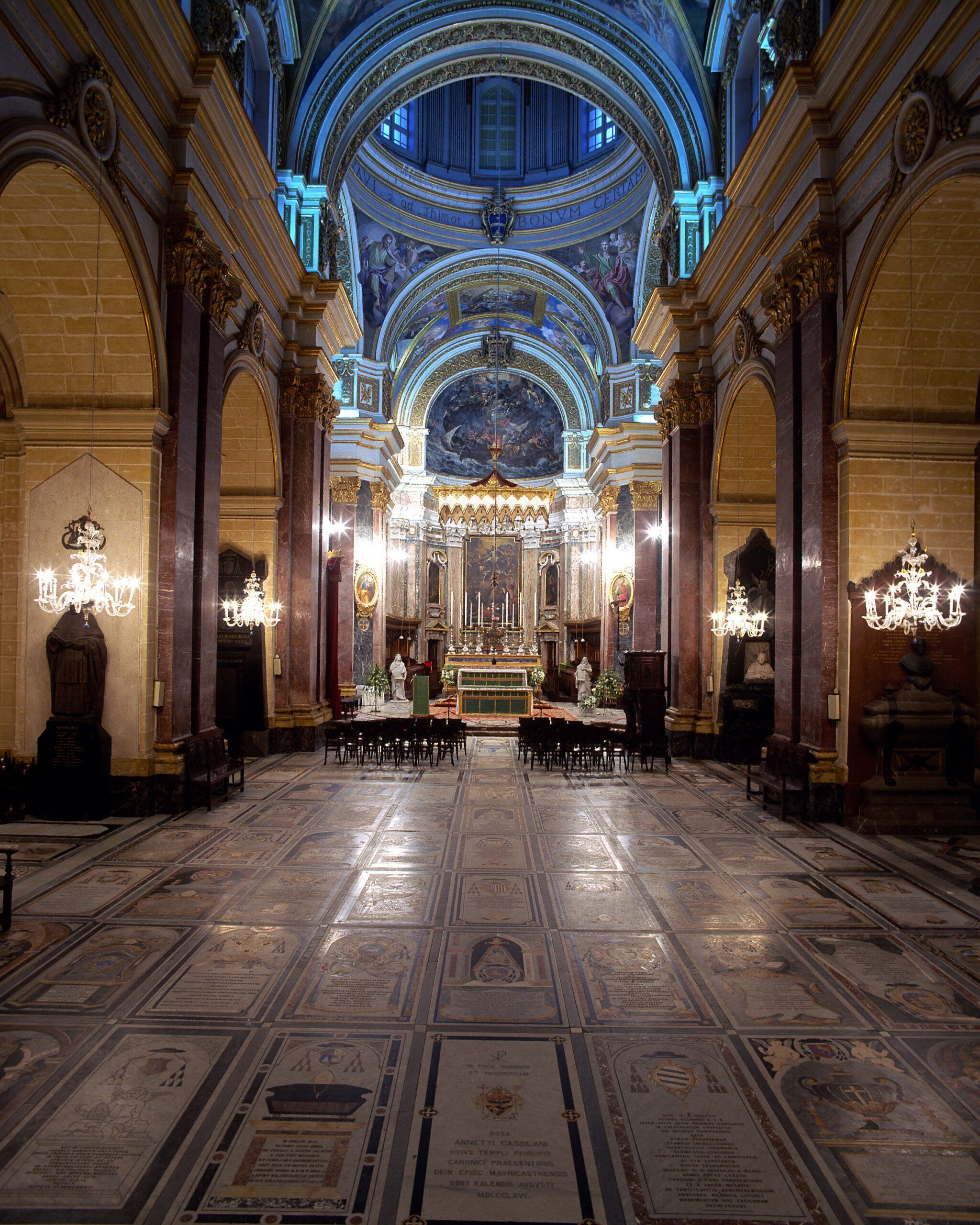 A grand hall with a high ceiling, ornate chandeliers, and a central altar.