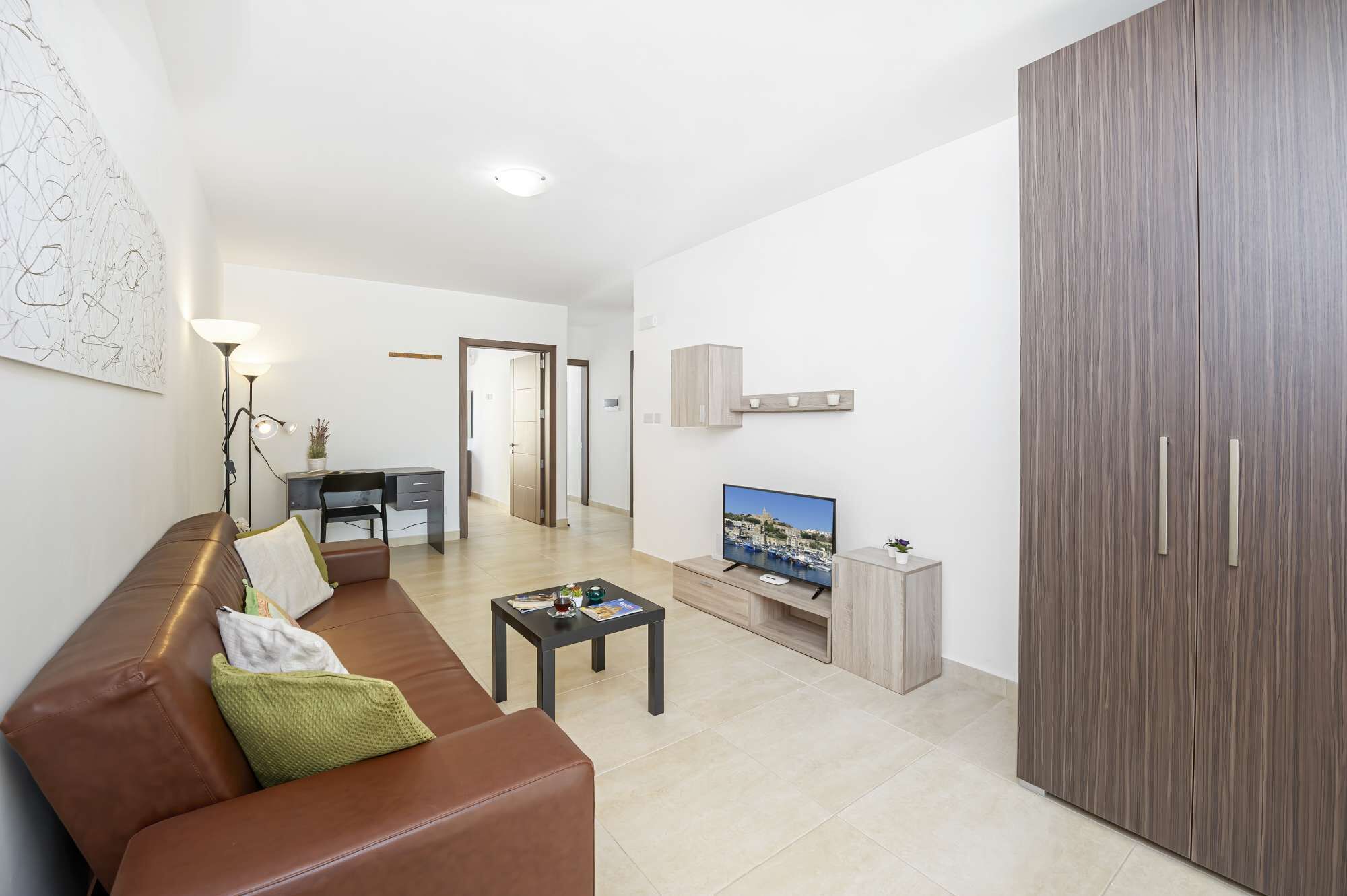 Una sala de estar moderna con un sofá de cuero marrón, una mesita de centro, un televisor y un armario.