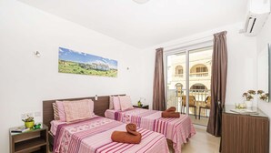 Ein Hotelzimmer mit zwei Betten, einem Balkon mit Blick auf ein Gebäude, einem Bild an der Wand und einem kleinen Tisch mit einer Pflanze.