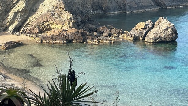 Paesaggio costiero con acque cristalline, formazioni rocciose e una spiaggia sabbiosa.