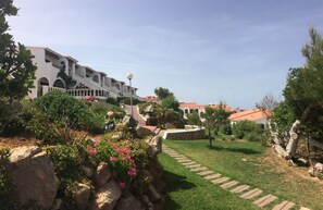 A landscaped garden with a stone pathway leading to a building with a red-tiled roof. - COSTA ARENAL 5 NEAR THE BEACH (Arenal d'en Castell)