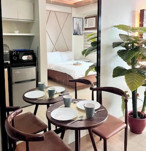 A compact room with a kitchenette, a bed, a dining area with chairs and a table, and a large potted plant. - Room-relax Stay at One Madison Tower (Iloilo)