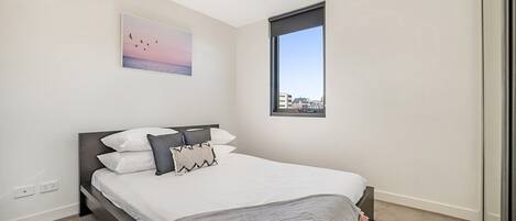 A modern bedroom with a large bed, a city view window, and a painting on the wall.