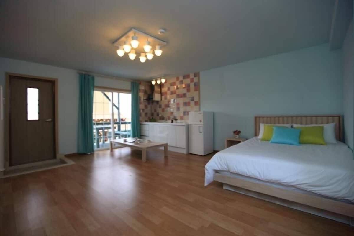 Una habitación con cama, una mesita, kitchenette y puerta corrediza a un balcón.
