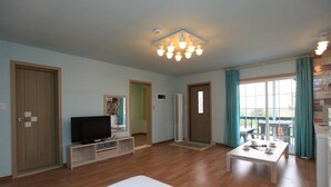 Een ruime woonkamer met een flatscreen televisie, een houten salontafel en een groot raam met gordijnen.