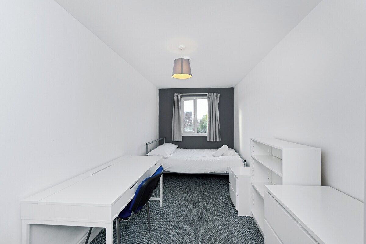 A small, modern hotel room with a single bed, a desk, and a chair.