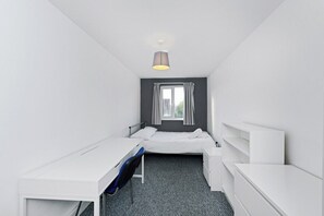 Une petite chambre d’hôtel moderne, équipée d’un lit simple, d’un bureau et d’une chaise.