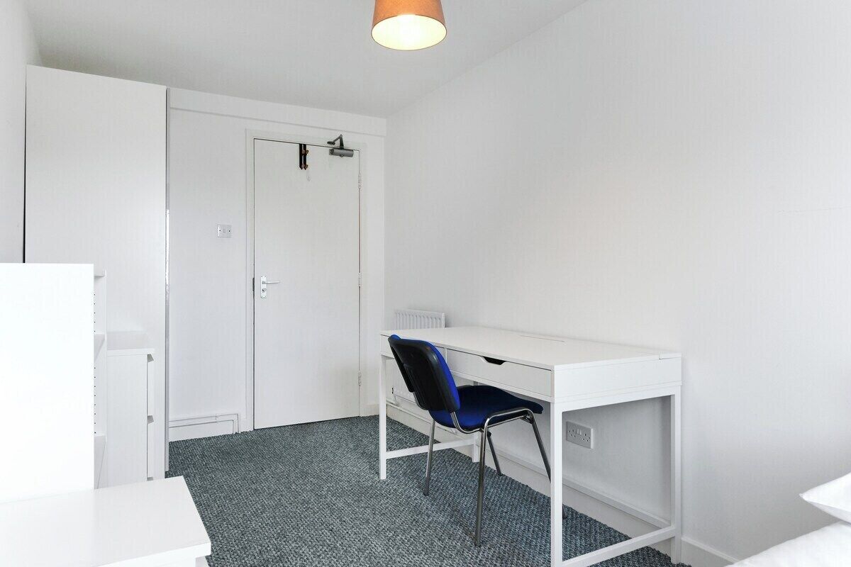Una habitación con un escritorio blanco, una silla azul, un radiador blanco y un armario blanco.