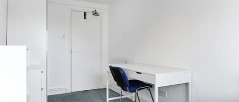 Una habitación con un escritorio blanco, una silla azul, un radiador blanco y un armario blanco.