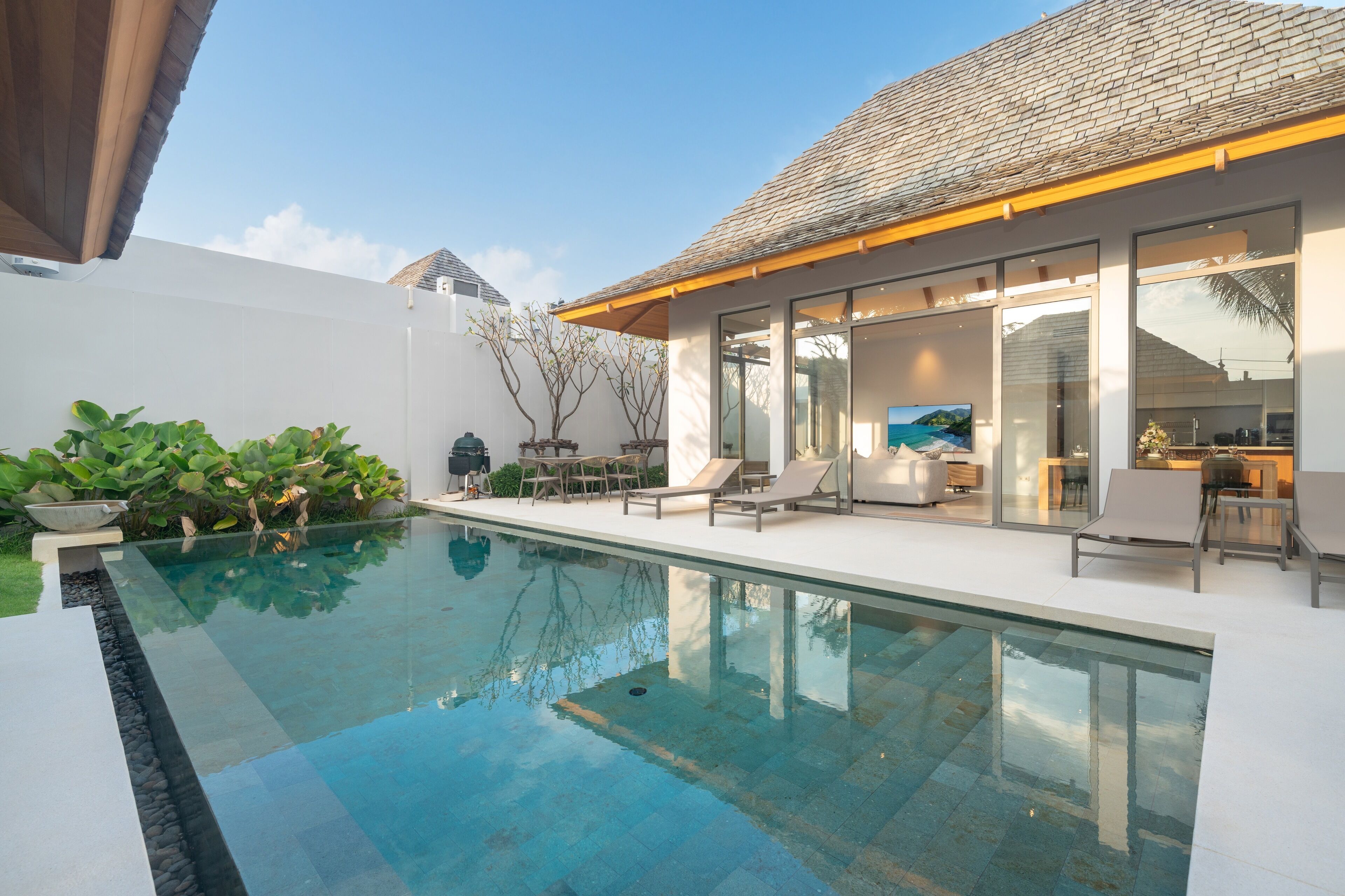 Una casa moderna con piscina, zona de estar exterior y cocina a la vista.