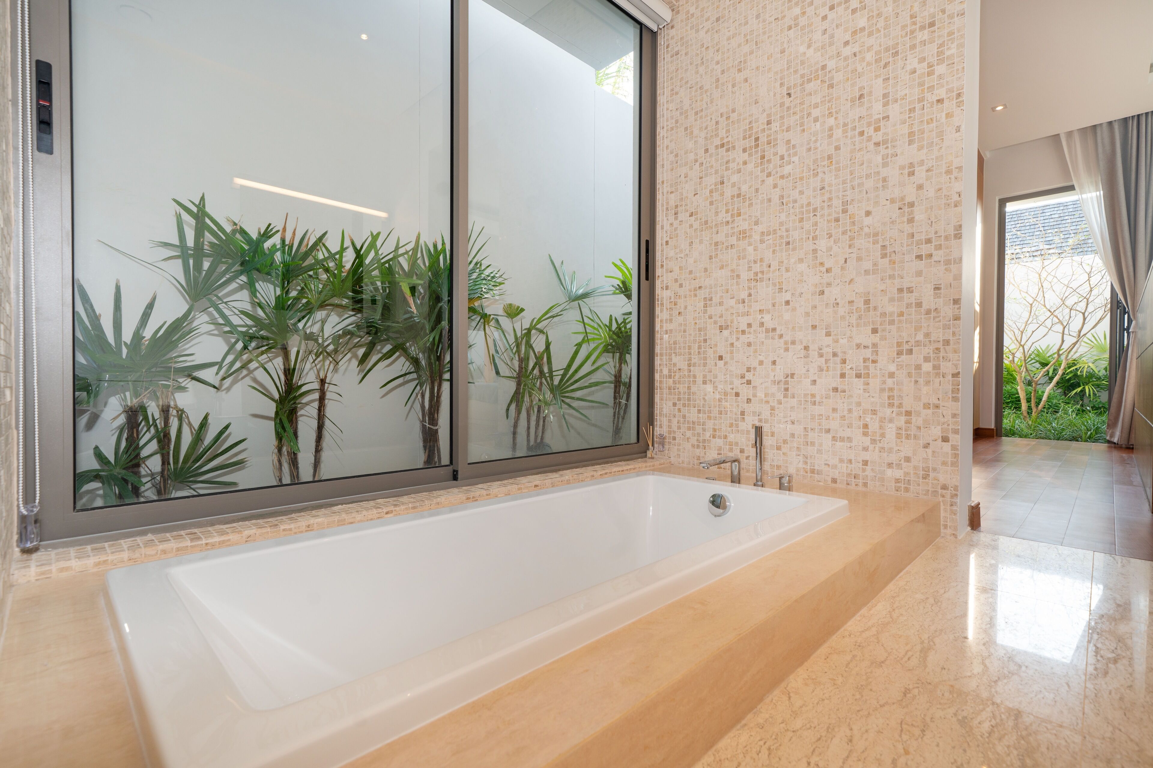 A modern bathroom with a large bathtub, a glass shower enclosure, and a view of greenery outside.
