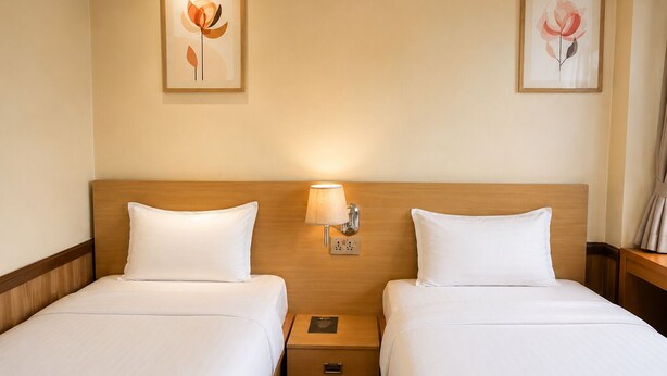 Quarto de hotel com duas camas, cabeceira de madeira, luminárias laterais e quadros nas paredes.