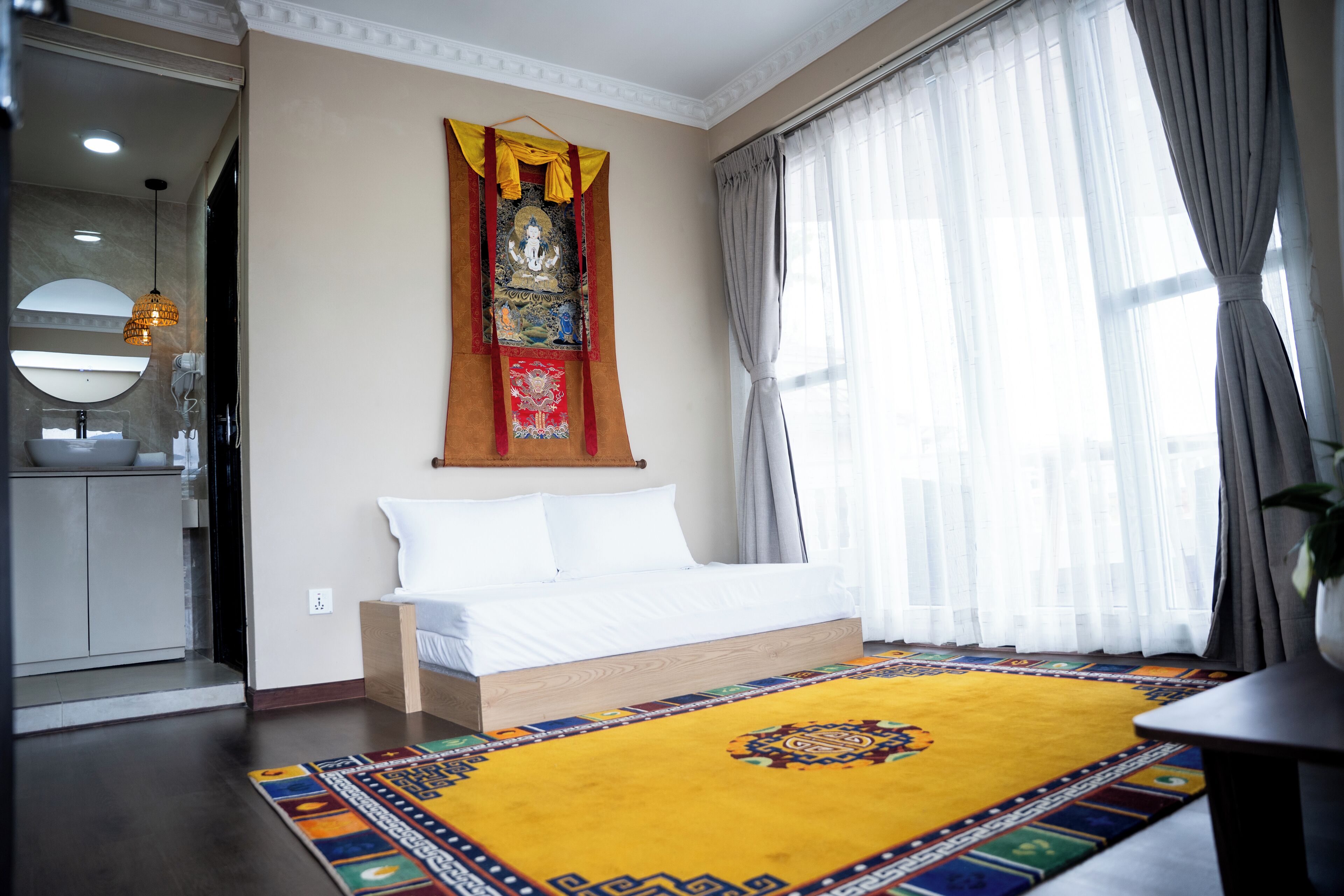 Habitación de hotel con cama, un ventanal con cortinas, un tapiz colgado en la pared y una alfombra colorida.