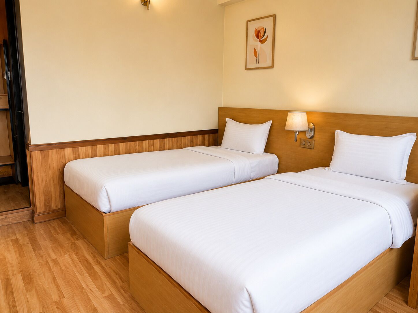 A hotel room with two single beds, wooden headboards, a wall-mounted lamp, and a framed picture.