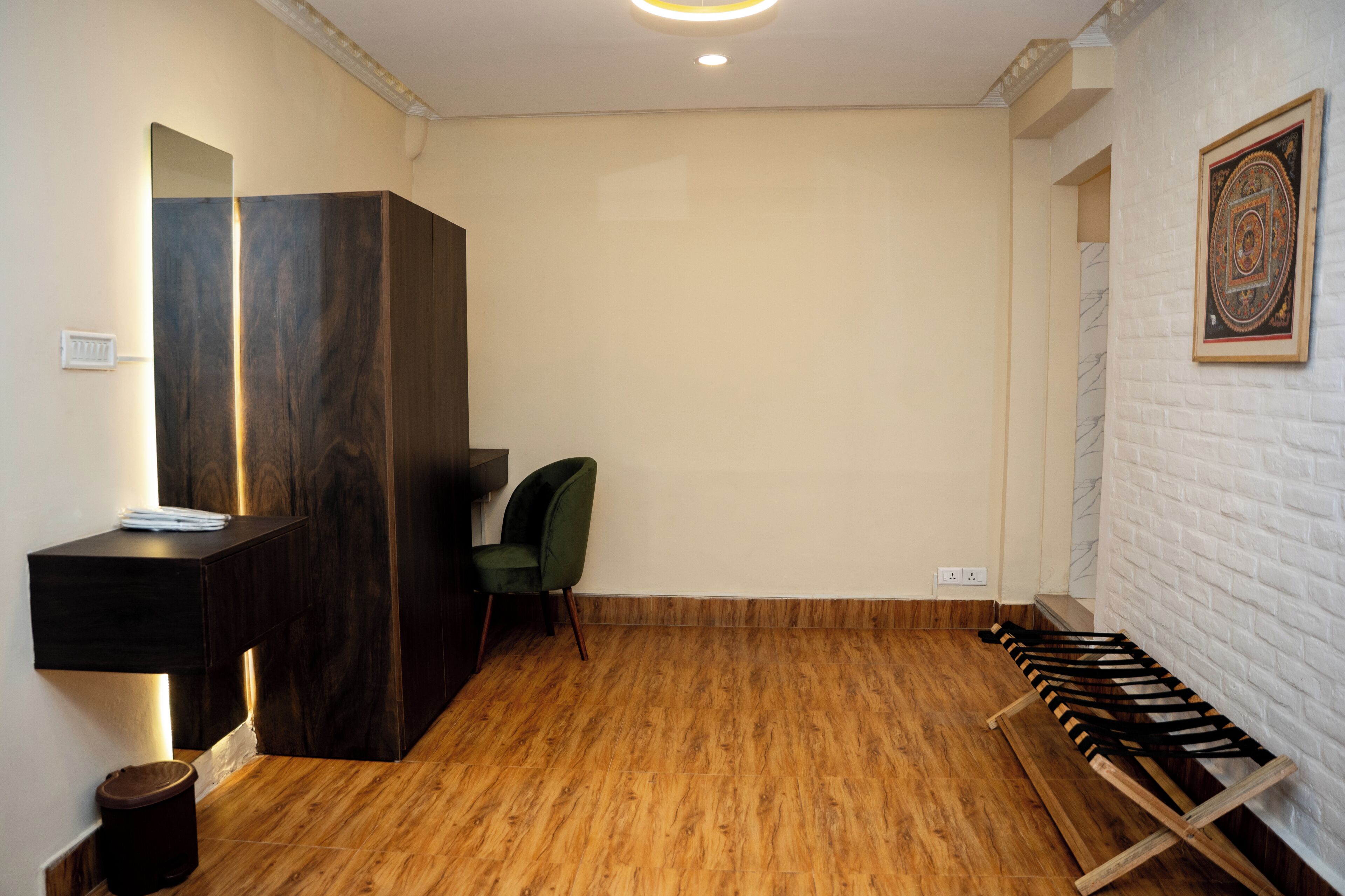 A room with a wooden floor, a dark wooden cabinet, a green chair, and a white brick wall with a framed picture.