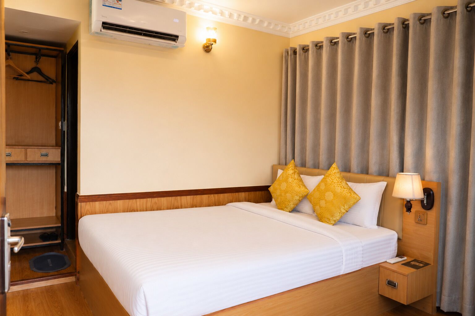 Habitación de hotel con cama, mesita de noche, lámpara, armario y equipo de aire acondicionado.