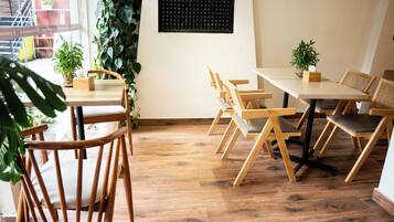 Un coin repas en bois avec des tables et des chaises, un mur noir orné d’un motif quadrillé et des plantes vertes.