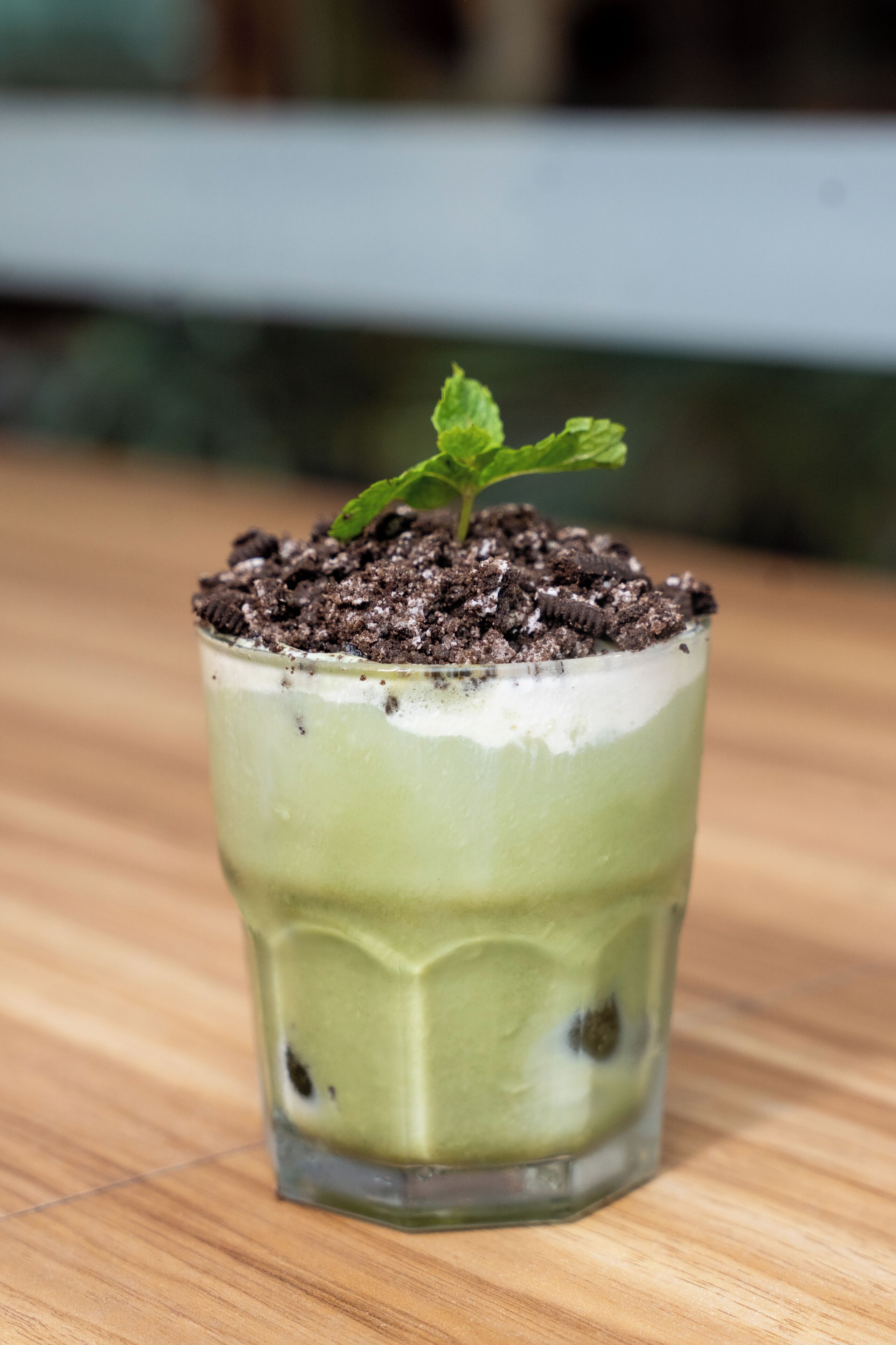 A glass with a layered drink, topped with soil and a sprouting plant.