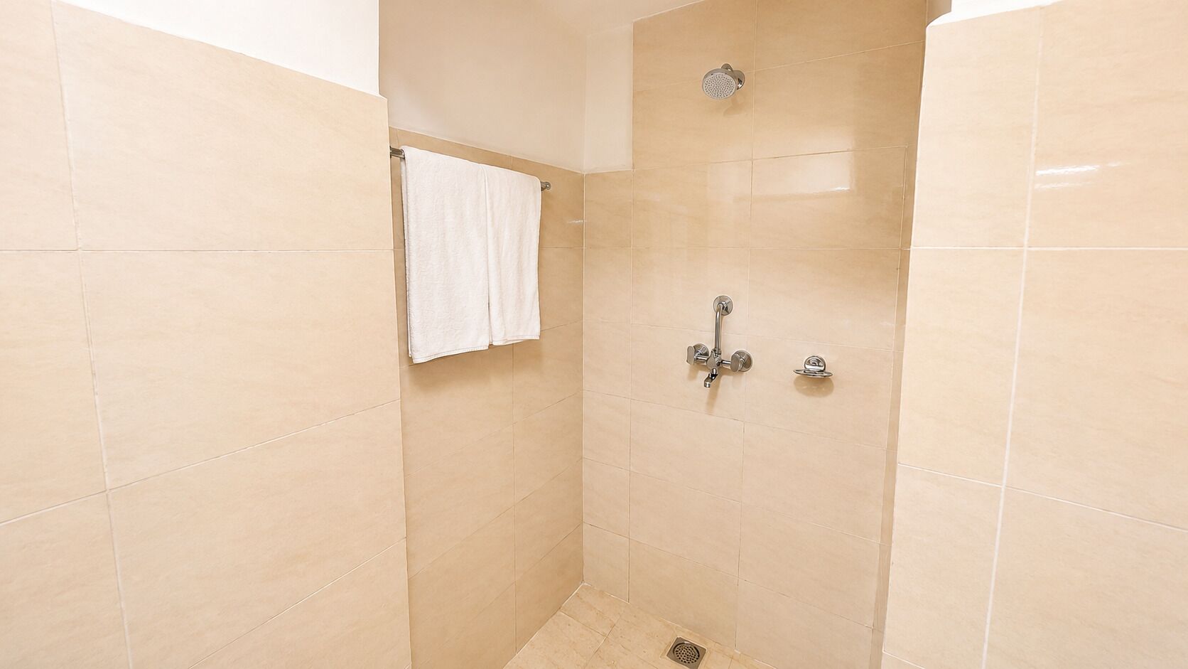 A shower with beige tiles, a white towel hanging on the wall, and a showerhead.
