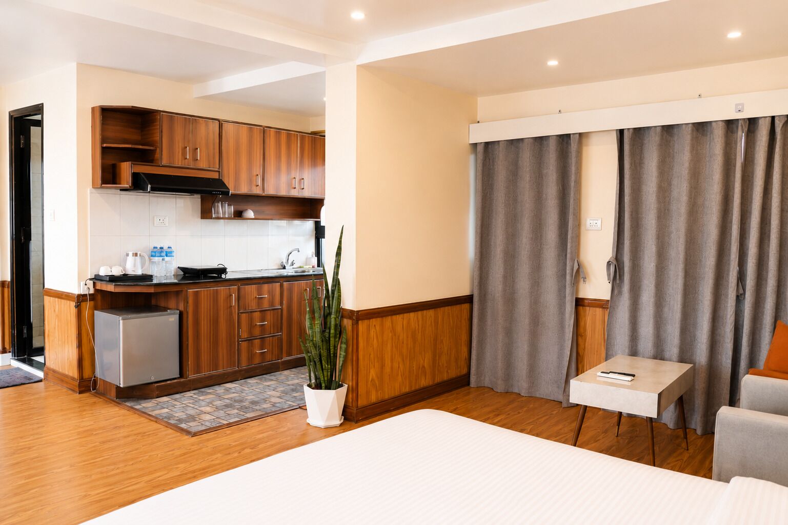 Une chambre d’hôtel équipée d’une kitchenette, d’un lit, d’une petite table et d’une plante en pot.