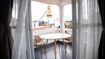 Ein offener Balkon mit rundem Tisch und Stühlen, Blick auf ein Gebäude mit einem Turm und einem klaren Himmel.