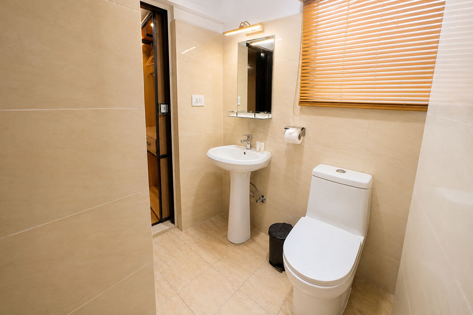 A bathroom with a toilet, sink, mirror, and a trash bin.