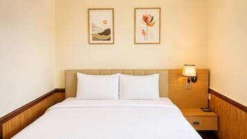 A hotel room with a bed, two framed artworks on the wall, a nightstand with a lamp, and a wooden headboard.