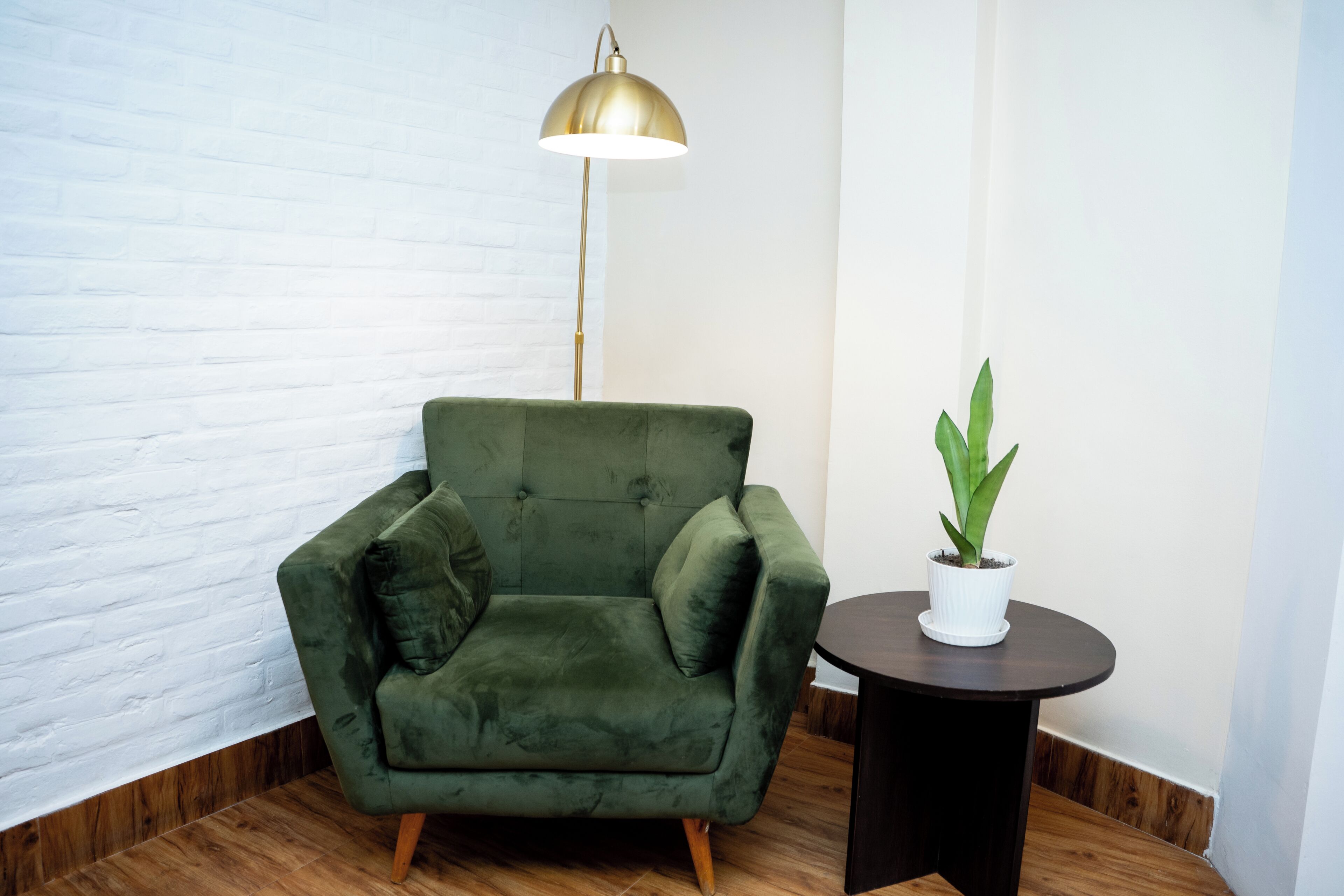 A room with a green armchair, a round table with a potted plant, and a floor lamp.