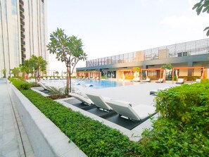Un hôtel moderne doté d’une piscine sur le toit, de chaises longues et d’un jardin bien entretenu.