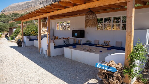 Un área de estar al aire libre techada con una televisión, vigas de madera y un cartel que dice 'Goat door'.