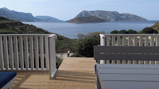 Una terraza de madera con barandillas blancas, con vistas a un mar tranquilo y montañas distantes.