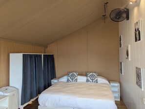 Un dormitorio con cama, armario, mesita de noche, ventilador y cuadros en la pared.