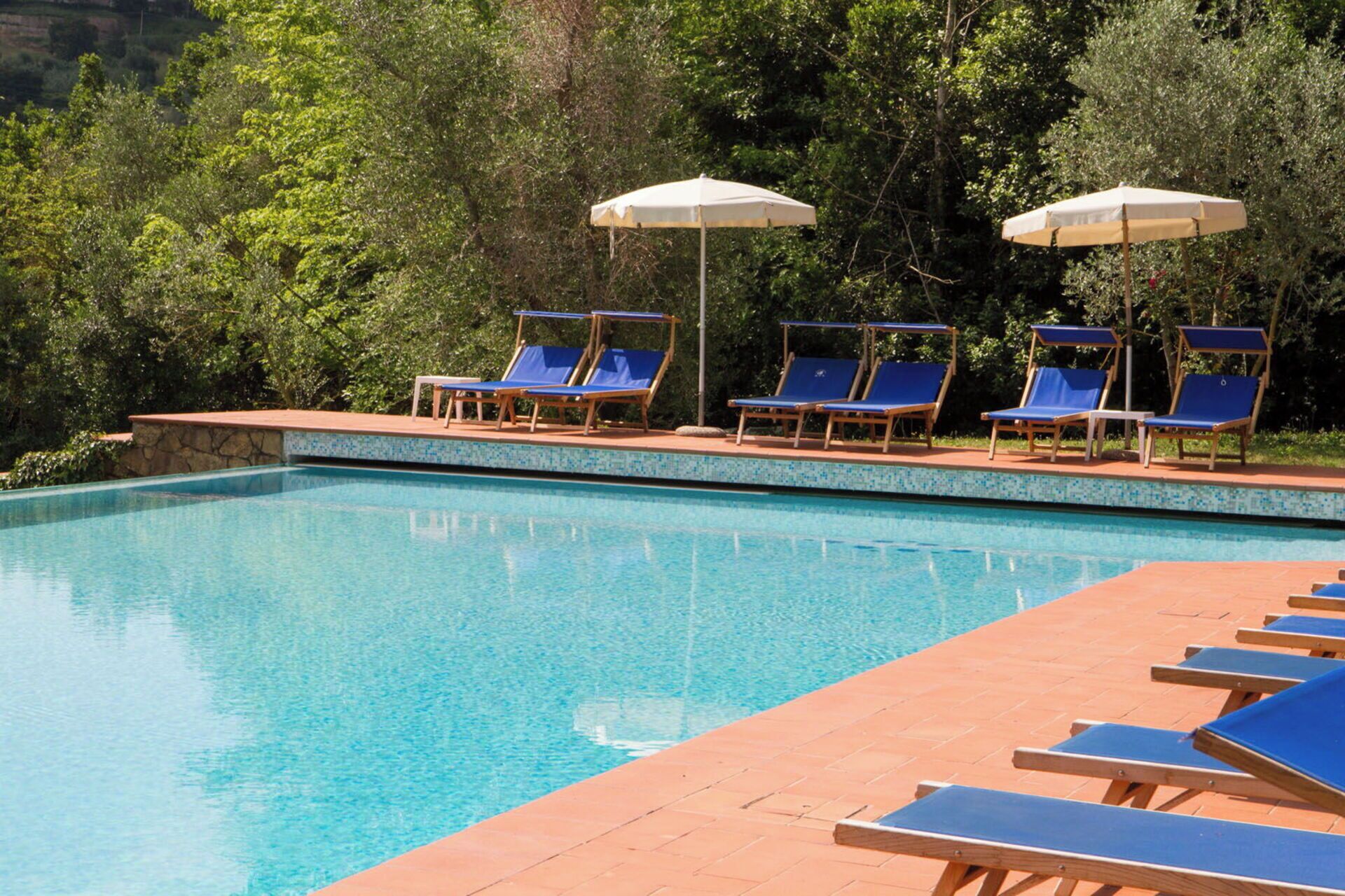 Una piscina con acqua cristallina, circondata da lettini e ombrelloni.