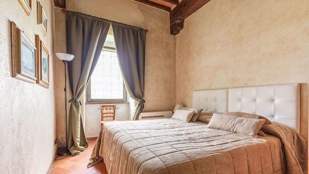 Une chambre à coucher avec un grand lit, une table de chevet, une chaise et une fenêtre avec des rideaux.