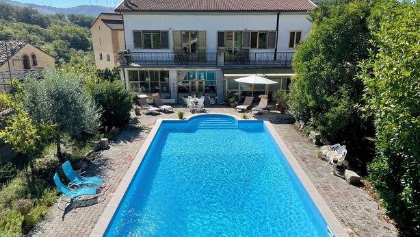 A rectangular swimming pool with clear blue water, surrounded by a paved patio with lounge chairs and a table. - Luxurious Mountain Villa With Pool in Fairytale-like Puglia (Roseto Valfortore)