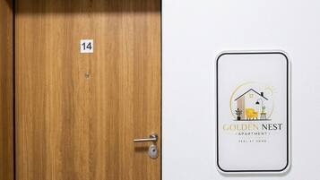 Una puerta de madera con una placa de número, un letrero en la pared que dice 'Golden Nest Apartment' y un interruptor de luz.