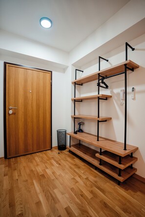 Ein Zimmer mit Holztür, einer an der Wand befestigten Regalwand und einem Mülleimer.