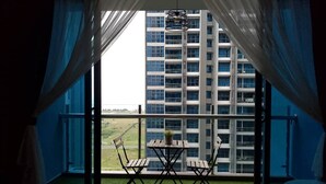 Ein Balkon mit Tisch und Stühlen und Blick auf ein Hochhaus, mit leichten Vorhängen.