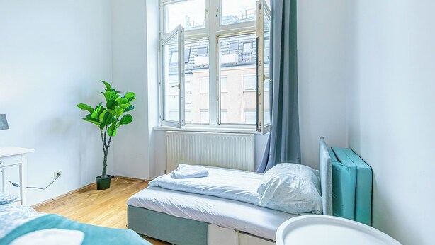 A small, bright room with a single bed, a potted plant, and a window overlooking buildings. - Stylish 1BR Apartment In Vienna Center (Vienna)