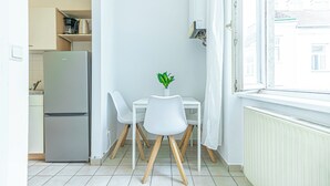 A small kitchen with a refrigerator, a dining table with two chairs, and a window with a view of buildings. - Stylish 1BR Apartment In Vienna Center (Vienna)