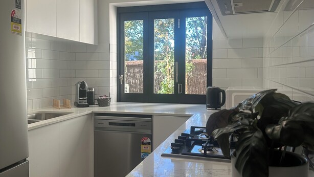 Een moderne keuken met witte kastjes, een ingebouwde vaatwasser, een gasfornuis en een raam met uitzicht.