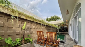 A patio with two wooden chairs, a small table, and a concrete wall with plants. - Ingrid Villa Ubud by AGATA (Ubud)
