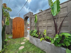 A courtyard with a wooden gate, a concrete wall, and lush green plants. - Ingrid Villa Ubud by AGATA (Ubud)