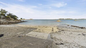 Een strand met een betonnen pad dat naar het water leidt, een rotsachtige kustlijn en een heldere lucht.