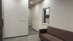 A hallway with textured walls, a brown sofa, and a window with a reflection. - Hotel Kajal Inn (Ajmer)